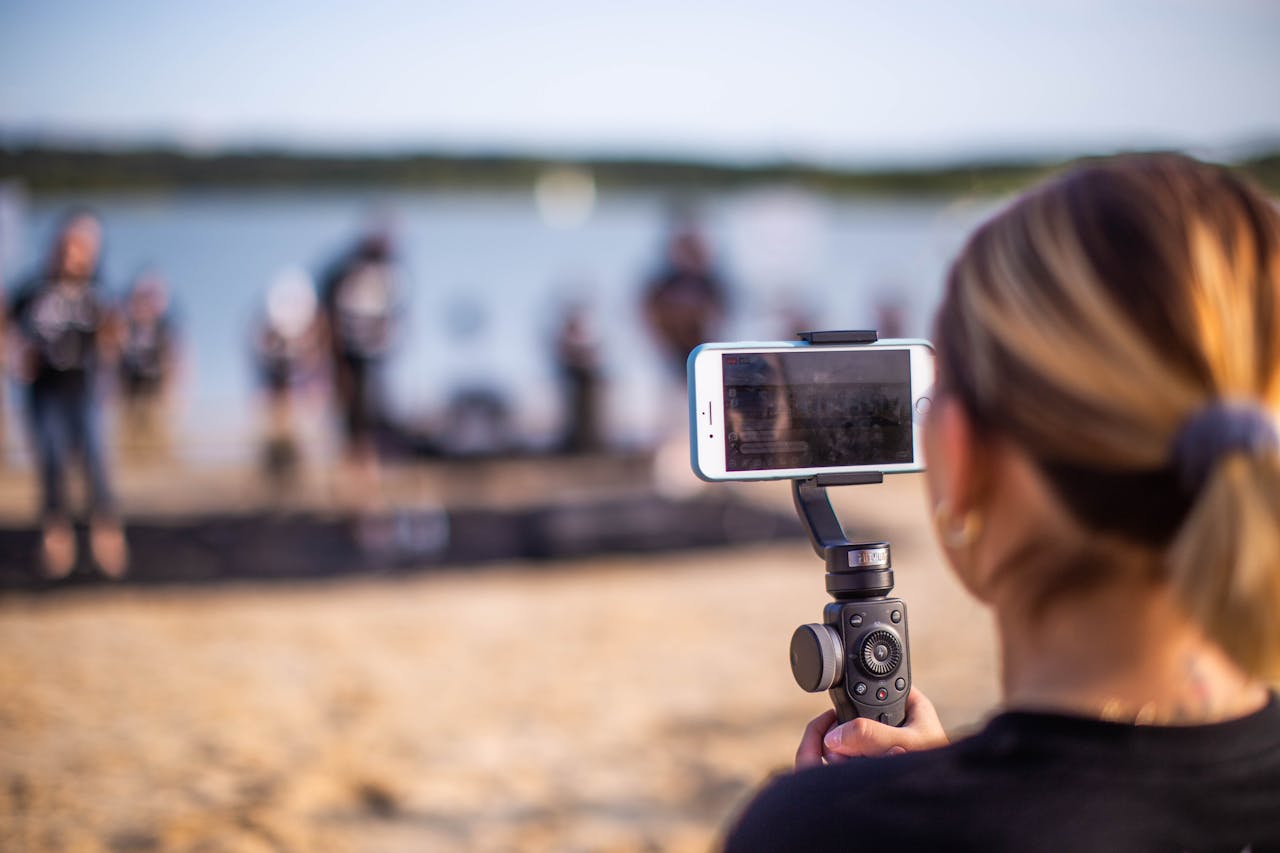 hero-img-01 Woman using a smartphone on a monopod to record a beach event.